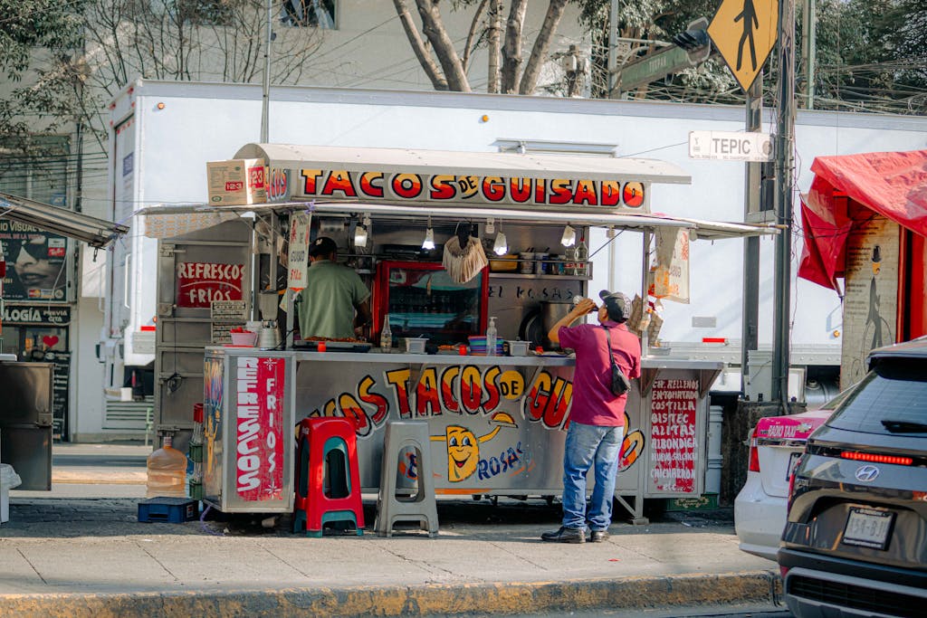 A bustling street vendor selling tacos in a colorful open-air stall on a sunny day.